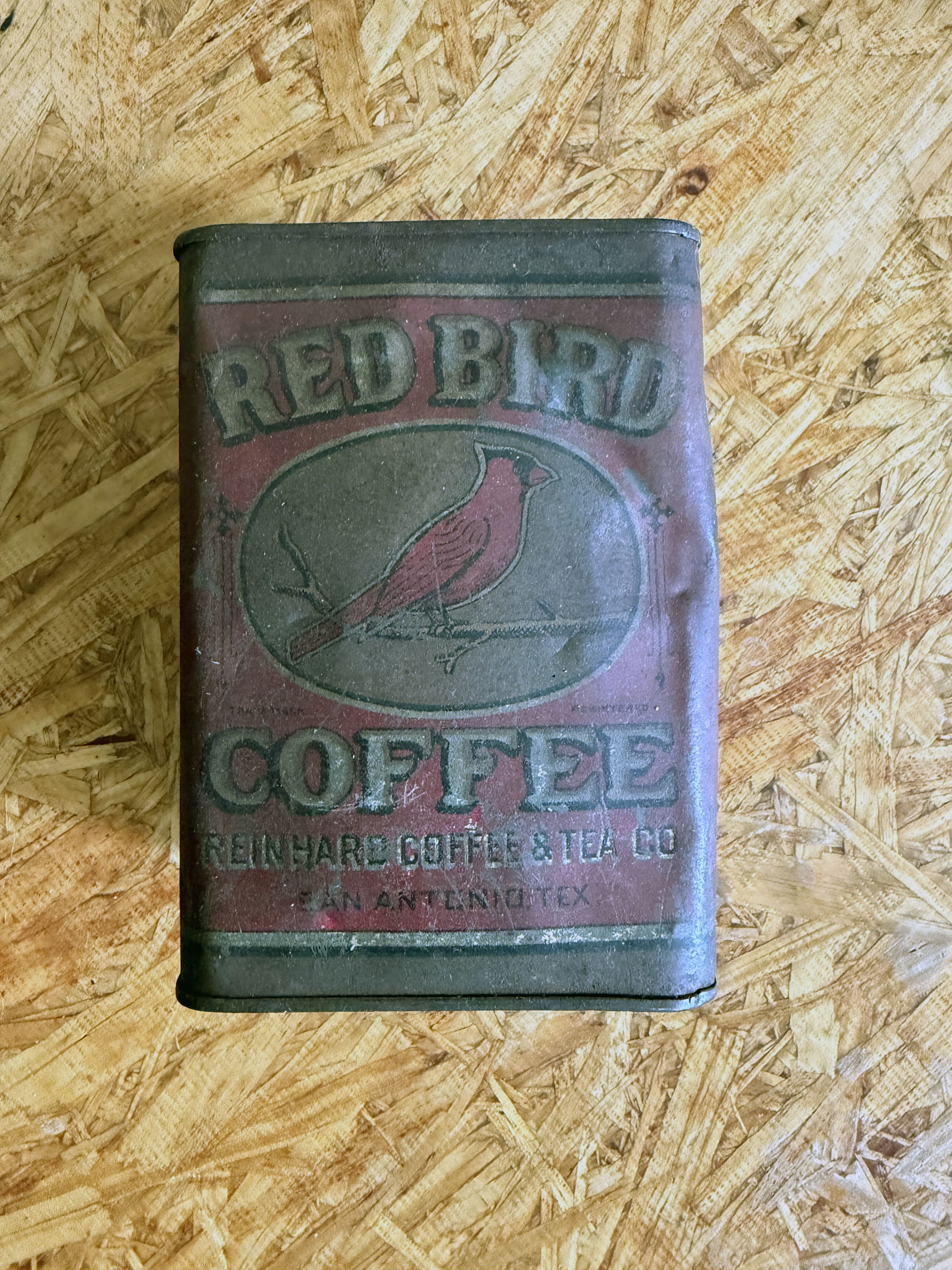 Front panel of the Red Bird one-pound tin: arched RED BIRD lettering, cardinal illustration in an oval frame, COFFEE in block capitals, and REINHARD COFFEE & TEA CO. / SAN ANTONIO, TEX. along the base. Maroon field with dark trim; tin shows age and a dent at the right edge.