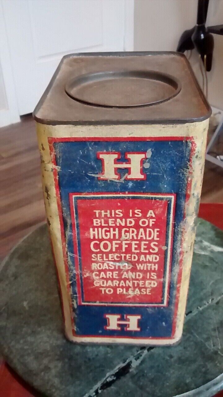 Color photograph documented 2023-05-20 of the same large square-cross-section bulk-size H and H Blend Coffee tin photographed square-on to its opposite broad face — a deep blue field framed by a red double-line border on a cream ground, with smaller red cartouches each carrying a single cream serif 'H' centered above and below, and at the center of the panel a large red rectangular cartouche carrying the firm's full early product guarantee in cream serif capitals: 'THIS IS A / BLEND OF / HIGH GRADE / COFFEES / SELECTED AND / ROASTED WITH / CARE AND IS / GUARANTEED / TO PLEASE'; the unpainted square top with its circular recessed lid well visible above (lid missing).