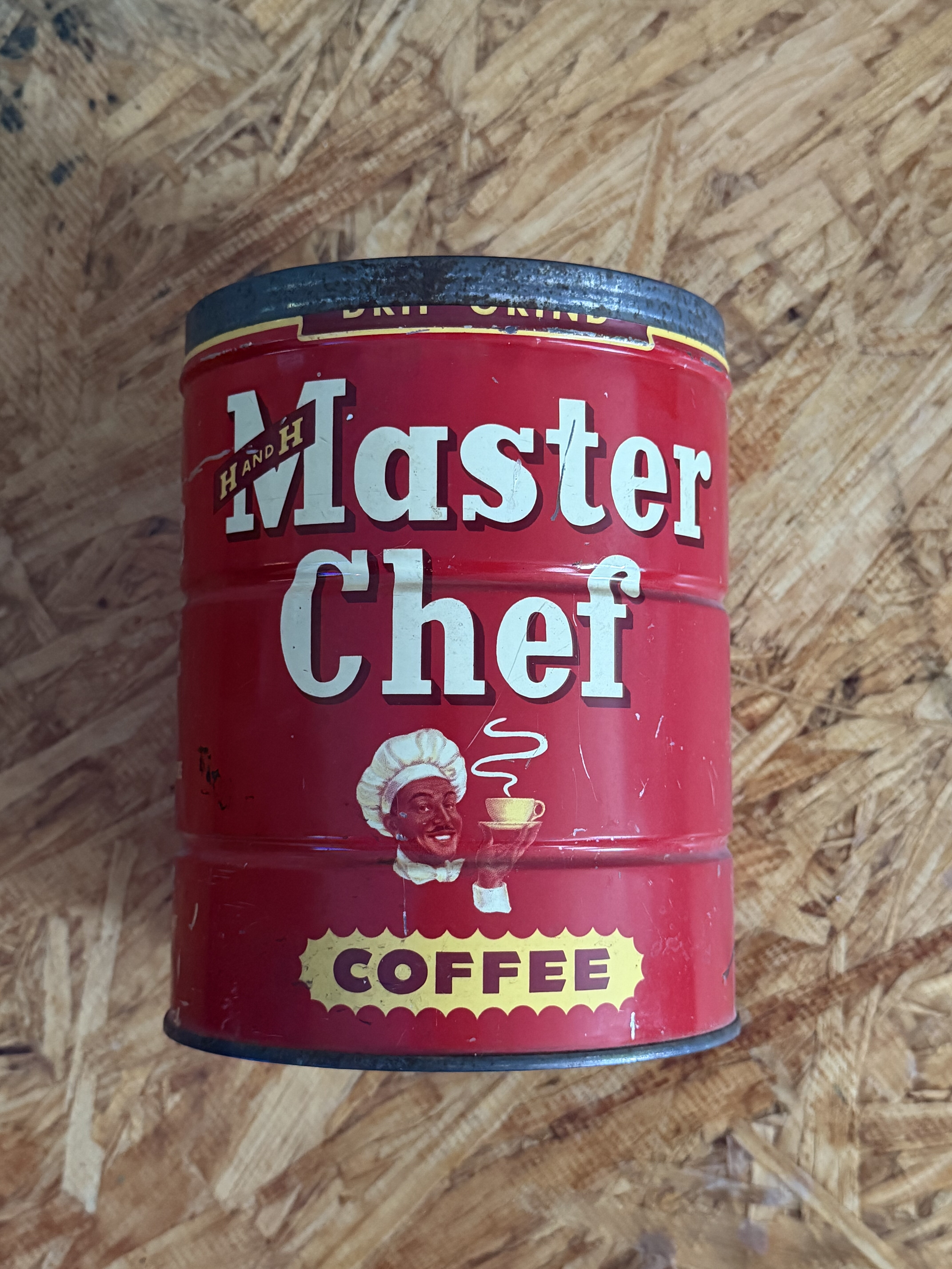 Master Chef two-pound keywind tin #2 — earlier white-script livery, script 'Master Chef' lettering on red with chef-portrait roundel and yellow oval 'COFFEE' badge, H AND H diamond at lower left, photographed 2026-05-23 on the workshop OSB benchtop