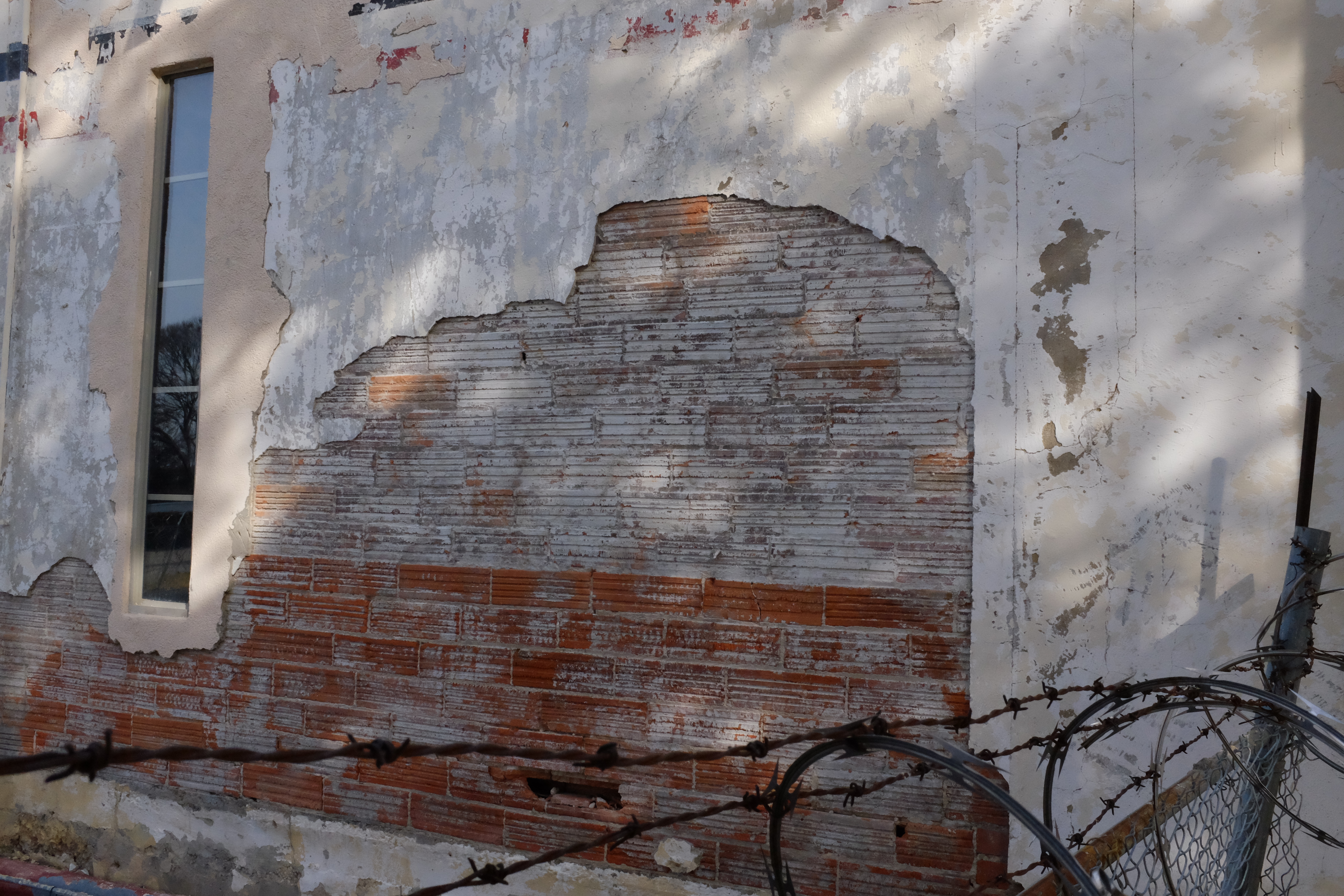 South-face clay tile — wide stucco failure above fence line