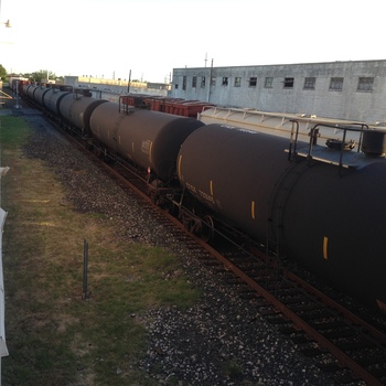 **10 June 2014** (**Apple iPhone 5**) — oblique **high view** along the **siding**: string of black **GTCX** tank cars (**733145** visible), parallel grey **concrete** industrial block, ballast and grass; long shadows — same **rail context** as other gallery trackside frames.