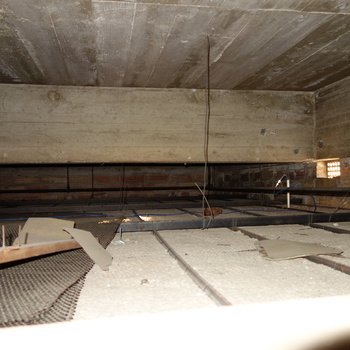 **5 October 2014** (**Sony DSC-RX100**) — confined **plenum or ceiling void**: heavy **concrete slab** above, **brick end wall** with small **glass block / vent** penetrations, **black** service pipe, **suspended** grid with **fibrous panels**, **diamond mesh** scrap — flash-lit interstitial at Hoffmann-Hayman.