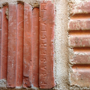Close-up of structural clay tile or hollow-tile coursework in the Hoffmann-Hayman factory masonry, photographed 24 October 2014 (iPhone 5) — terracotta-red extruded units bedded in coarse buff-grey mortar, one vertical tile face carrying a raised manufacturer stamp reading **FRASER CLAY** in vertical capitals, with horizontal ribbing visible on an adjoining unit — the same hollow structural clay tile family already visible in cross-section in the [second-floor expansion hole through the 1932 exterior wall](/assets/images/gallery/factory-upstairs-expansion-hole-through-original-exterior.jpg), here documented in situ with a readable supplier mark