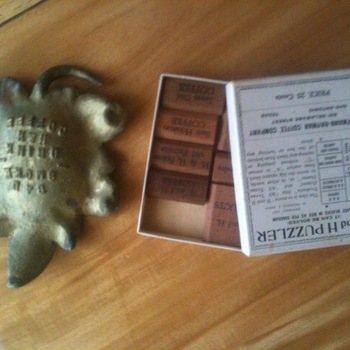 Overhead project photograph 3 July 2015 on wood — left: cast leaf-shaped metal ashtray premium with embossed words Eat, Smoke, Drink, H and H, Coffee in a ring around the bowl; right: open 1927 H and H Puzzler game box, lid printed Hoffmann-Hayman Coffee Company, 601 Delaware Street, San Antonio, Texas, price 25 cents, copyright 1927, with wooden sliding blocks showing Texas Girl Coffee, San Antonio Coffee, H and H Coffee, H and H Spices and Extracts, H and H Products — companion field shot to the gallery still of the box lid alone