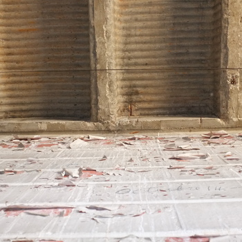 **1 August 2015** (**Fujifilm FinePix X100**) — tight view: **corrugated-pan concrete ceiling** bays meeting a **peeling white** wall with red brick showing through; faint **October 14** pencil graffito — **pan-formed floor/ceiling** finish consistent with the **1930s expansion** shell.