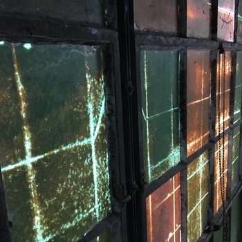 **25 February 2016** (**Apple iPhone 6s**) — abstract tight frame on **aged wire-laminated or heavy-rolled** glass in **steel-sash** factory windows, **chain** hardware at margin; green-amber patina and backlight — Hoffmann-Hayman **industrial glazing** documentation.