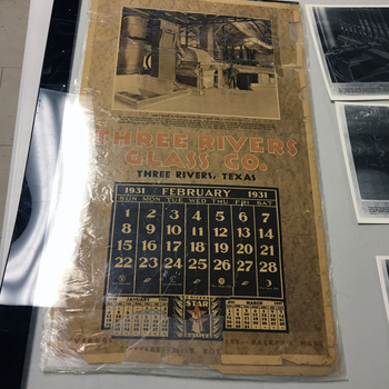 **Color photograph** taken **April 2017** at the **Three Rivers Glass Co.** collectors’ weekend — **large-format promotional wall calendar** from **Three Rivers Glass Co., Three Rivers, Texas**, with a central **February 1931** month grid, **January** and **March 1931** strips at the foot flanking a **3 RIVERS STAR BOTTLES** logo, and a top panel **factory-interior** photograph captioned **HERE'S WHERE GLASS SAND STARTS ON A THREE AND A HALF DAY TRIP** with supporting copy on batch ingredients and **125-ton** furnace capacity; bottom strip lists beverage bottles, milk bottles, and packers ware — **show-field documentation** of TRGCo advertising ephemera (**not** an object in the San Antonio museum collection)