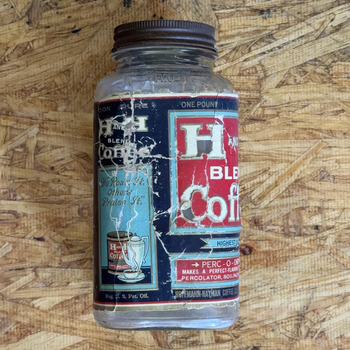 H and H Blend Coffee one-pound smooth-body Crystalvac jar whose paper label is a reassembled composite — heavily crackled fragments laid out of alignment, showing the light-blue We Roast It Others Praise It side panel with its coffee pot and cup vignette beside the red H and H Blend cartouche, photographed 2026-07-21