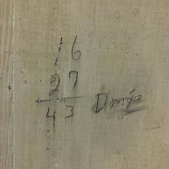**Second-floor post-1932 expansion inventory** bay at the Hoffmann-Hayman factory (per site note: same **storage / loading** zone as the **November 2015** **[fork punctures](/assets/images/gallery/2015-11-24-factory-second-floor-expansion-west-wall-forklift-fork-punctures.jpg)** and **brick tally** frames) — close-up of a **vertical-grain wood** face (**door or partition**) under **aged off-white / beige paint** with flecked grime and soft wear — **graphite pencil** exercise scratched on the boards: stacked numerals **16** above **27**, **sum line**, total **43**; at **right** a flowing inked or pencil **cursive** personal name read here as **Donje** — **idle arithmetic and signature** left on **millwork** beside the **trades’ stock math** already documented on **[exposed brick](/assets/images/gallery/2015-11-24-factory-second-floor-inventory-room-brick-stock-tally.jpg)** in this room — **Instagram** media export **17975885107093877**