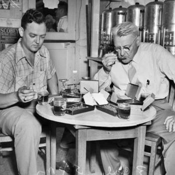 Gus P. Menger and son Albert tasting coffee at a cupping table with H and H Coffee silos in the background — San Antonio Light Photograph Collection, UTSA Libraries Special Collections