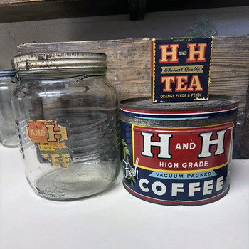 Three H and H products staged together — a clear-glass Crystalvac drip-grind coffee jar with torn paper label, a 3 oz H and H Tea (Orange Pekoe and Pekoe) cardboard box, and a one-pound H and H High Grade Vacuum Packed Coffee keywind tin